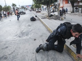 In this Dec. 2014 handout photo provided by Cristopher Rogel Blanquet, a federal police officer attempts to pull himself up onto a sidewalk after being injured in a clash with protesters in Chilpancingo, Mexico. This photo was not taken in confrontations with migrants making their way in a caravan from Central America to the U.S., despite a post circulating on social media.