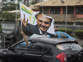 A supporter waves a flag with an image of Jair Bolsonaro as he drives past in front of his residence in Rio de Janeiro, Brazil, Monday, Oct. 29, 2018. Far-right congressman Bolsonaro won Brazil's presidency Sunday on promises to overhaul several aspects of Latin America's largest nation.