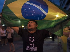 A man sing the Brazil's national anthem as he waves the national flag in support leading presidential candidate Jair Bolsonaro, outside Bolsonaro's residence in Rio de Janeiro, Brazil, Saturday, Sept. 29, 2018. Bolsonaro, who suffered intestinal damage and severe internal bleeding after the Sept. 6 attack at a campaign event and has undergone multiple surgeries, was discharged Saturday from a Sao Paulo hospital where he was being treated.