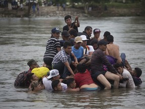 A group of Central American migrants cross the Suchiate River aboard a raft made out of tractor inner tubes and wooden planks, on the the border between Guatemala and Mexico, in Ciudad Hidalgo, Mexico, Saturday, Oct. 20, 2018. After Mexican authorities slowed access through the border bridge to a crawl, hundreds of migrants are boarding the rafts or wading across the river and crossing into Mexico illegally.