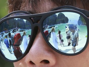 In this Thursday, May 31, 2018, photo, tourists are reflected in sunglasses on Maya Bay on Phi Phi island in Krabi province, Thailand. Maya Bay will close to tourists indefinitely until its ecosystem returns to its full condition, the Department of National Parks, Wildlife and Plant Conservation said in a Monday announcement published on the Royal Gazette.