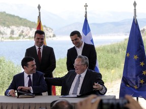 FILE - In this Sunday, June 17, 2018, file photo, Greek Prime Minister Alexis Tsipras, background right, and his Macedonian counterpart Zoran Zaev, background left, look on as Greek Foreign Minister Nikos Kotzias, right, and his Macedonian counterpart Nikola Dimitrov sign an agreement on Macedonia's new name in the village of Psarades, Prespes Greece. Greek Foreign Minister Nikos Kotzias resigned Wednesday, Oct. 17, 2018, following a disagreement with the defense minister over the handling of a recent deal which would change Macedonia's name in exchange for Greece dropping its objections to the country joining NATO.