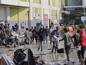 People carry items from the shopping mall which was damaged following earthquakes and tsunami in Palu, Central Sulawesi, Indonesia, Sunday, Sept. 30, 2018. Rescuers try to reach trapped victims in collapsed buildings after hundreds of people are confirmed dead in a tsunami that hit two central Indonesian cities, sweeping away buildings with massive waves.