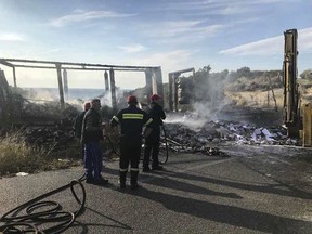 Firefighters spray water on the debris of a truck following a collision near Greece's northern town of Kavala, Saturday, Oct. 13, 2018.  A speeding car carrying migrants collided with a truck in northern Greece on Saturday, killing 11 people, police said. (Proininews.gr via AP)