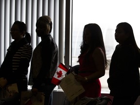 New Canadians wait their turn to pose for picture with Citizenship Judge Albert Wong after the conclusion of a citizenship ceremony held at Citizenship and Immigration Canada centre in Scarborough in Toronto, Ont.  on Tuesday December 23, 2014.