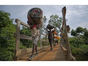 FILE - In this Thursday, June 8, 2017 file photo, from left to right, South Sudanese refugees Thomas Wani, 12, brother Peter Lemi, 14, mother Rose Sunday, and father Julius Lezu, cross a wooden bridge from South Sudan to Uganda at the Busia crossing, near Kuluba, in northern Uganda. An internal inquiry released in Nov. 2018 says the United Nations refugee agency has misspent millions of dollars on Africa's largest refugee crisis.