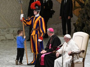 Pope Francis, right, and Prefect of the Papal Household, Georg Ganswein watch a boy who came from the audience onto the stage, play with a Swiss Guard's spear during the weekly general audience on November 28, 2018 at the Vatican.