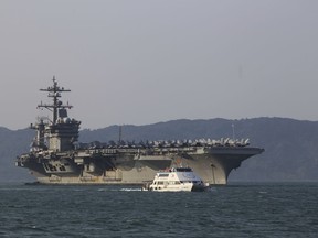 FILE - In this Monday, March 5, 2018, file photo, a Vietnamese passenger boat sails past U.S aircraft carrier USS Carl Vinson as it docks in Danang Bay, Vietnam. Over this last week, China demanded the United States stop sending ships and military aircraft close to its South China Sea island claims during talks to prepare for a meeting between President Donald Trump and President Xi Jinping later this month.