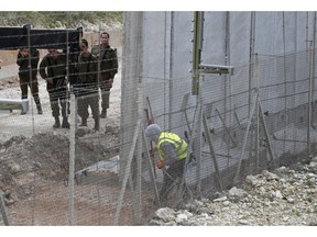 FILE - In this Feb. 8, 2018, file, photo, Israeli soldiers watch a construction worker building a wall along the Israeli border in the costal town of Naqoura, south Lebanon. Even with attention currently focused on Gaza-based Hamas militants along its southern border, Israel's most pressing security concerns lie to the north.