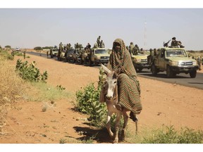 FILE - In this Thursday, Nov. 20, 2014 photo taken on a government organized media tour, a woman rides a donkey past a convoy of government troops in Tabit village in the North Darfur region of Sudan, where allegations surfaced of rape of women by government allied troops. Human Rights Watch is cautioning the United States against lifting its designation of Sudan as a state sponsor of terrorism. The New York-based watchdog said Thursday, Nov. 8, 2018 that Khartoum continues to violate basic human rights, with security forces regularly attacking civilians and opening fire on peaceful protesters.