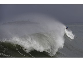 A man surfs near Fort Point in front of Alcatraz Island in San Francisco, Thursday, Nov. 29, 2018. A storm moving into California on Thursday brought rain that threatened to unleash debris flows in wildfire burn areas and snow that could cause travel problems in the Sierra Nevada.