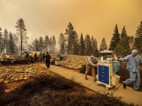 Medical workers move equipment from a makeshift emergency room while the Feather River Hospital burns as the Camp Fire rages through Paradise, Calif., on Thursday, Nov. 8, 2018. Tens of thousands of people fled a fast-moving wildfire Thursday in Northern California, some clutching babies and pets as they abandoned vehicles and struck out on foot ahead of the flames that forced the evacuation of an entire town.
