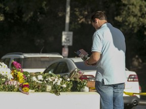 Brian White places a U.S. flag with a flower near the scene of a mass shooting Thursday, Nov. 8, 2018, in Thousand Oaks, Calif., after a gunman opened fire Wednesday evening inside a country music bar, killing multiple people including a responding sheriff's sergeant.