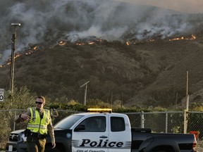A police officer directs traffic at a checkpoint in front of an advancing wildfire Thursday, Nov. 8, 2018, near Newbury Park, Calif. The Ventura County Fire Department has also ordered evacuation of some communities in the path of the fire, which erupted a few miles from the site of Wednesday night's deadly mass shooting at a Thousand Oaks bar.