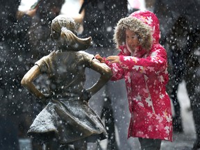 A young girl brushes snow off the Fearless Girl statue in lower Manhattan on Nov. 15, 2018, in New York. One of the first big storms of the season moved across the eastern half of the United States on Thursday.