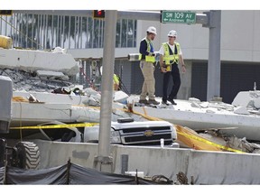 FILE - In a Sunday, March 18, 2018 file photo, inspectors walk over what remains of a pedestrian bridge near Florida International University, near Miami. Federal investigators said  in the two-page investigative update released Thursday, Nov. 15, 2018, that design flaws caused cracking in a pedestrian bridge that collapsed near Miami in March. The National Transportation Safety Board did not blame those errors for the March 15 collapse. Six people died in the collapse.