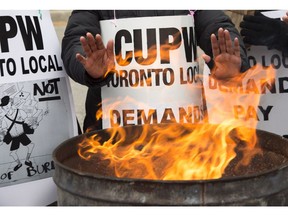 Striking Canada Post workers keep their hands warm as they picket at the South Central sorting facility in Toronto.