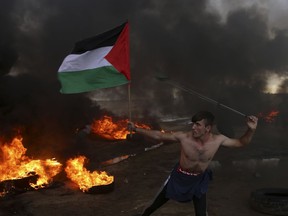In this Friday, Oct. 26, 2018 file photo, a protester hurls stones while holding the Palestinian flag amid burning tires near the fence of the Gaza Strip border with Israel during a protest.