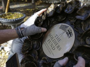 In this Wednesday, Nov. 7, 2018 photo James Re, of Boston, hands only, positions a bronze wreath as it becomes part of a memorial on the grounds of Old North Church, in Boston, that honors fallen soldiers from the U.S. and Britain. The memorial is being dedicated this month at an ironic venue - the Boston church where America's war for independence from England basically began. On Nov. 17, British and American military brass will unveil the bronze wreath and plaque at the church, saluting troops from both countries who have died in Iraq and Afghanistan.
