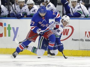 New York Rangers' Tony DeAngelo (77) and Vancouver Canucks' Jake Virtanen (18) fights for control of the puck during the first period of an NHL hockey game Monday, Nov. 12, 2018, in New York.