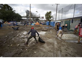 Men pick up trash as others bathe nearby, in a shelter for members of the migrant cavan in Tijuana, Mexico, Wednesday, Nov. 28, 2018. As Mexico wrestles with what to do with more than 5,000 Central American migrants camped out at a sports complex in the border city of Tijuana, President-elect Andres Manuel Lopez Obrador's government signaled Tuesday that it would be willing to house the migrants on Mexican soil while they apply for asylum in the United States -- a key demand of U.S. President Donald Trump.