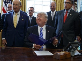 FILE - In this March 24, 2017 file photo, President Donald Trump, flanked by Commerce Secretary Wilbur Ross, left, and Energy Secretary Rick Perry, is seen in the Oval Office of the White House in Washington, during the announcing of the approval of a permit to build the Keystone XL pipeline, clearing the way for the $8 billion project.A federal judge in Montana has blocked construction of the $8 billion Keystone XL Pipeline to allow more time to study the project's potential environmental impact. U.S. District Judge Brian Morris' order on Thursday, Nov. 8, 2018,  came as Calgary-based TransCanada was preparing to build the first stages of the oil pipeline in northern Montana. Environmental groups had sued TransCanada and The U.S. Department of State in federal court in Great Falls.