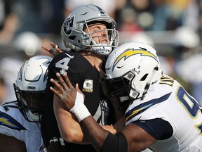 Oakland Raiders quarterback Derek Carr (4) is hit between Los Angeles Chargers linebacker Uchenna Nwosu, left, and defensive tackle Corey Liuget during the first half of an NFL football game in Oakland, Calif., Sunday, Nov. 11, 2018.