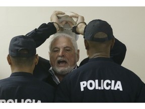 Panama's former President Ricardo Martinelli answers journalists questions as he raises his handcuffed hands, holding a book, while escorted by police to a hearing at the Supreme Court in Panama City, Monday, Nov. 19, 2018. Martinelli, who was president from 2009 to 2014, is accused of embezzlement and illegally monitoring phone calls and other communications. He has denied the charges.