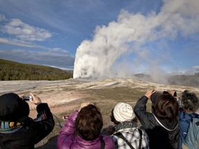 FILE - In this May 21, 2011, file photo, tourists photograph Old Faithful erupting on schedule late in the afternoon in Yellowstone National Park, Wyo. A 27-year-old Colorado man who walked dangerously close to Old Faithful geyser in September 2018, is banned from Yellowstone and Grand Teton national parks for five years.