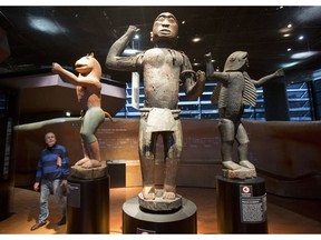 A visitors look at wooden royal statues of the Dahomey kingdom, dated 19th century, today's Benin,at Quai Branly museum in Paris, France, Friday, Nov. 23, 2018. From Senegal to Ethiopia, artists, governments and museums are eagerly awaiting a report commissioned by French President Emmanuel Macron on how former colonizers can return African art to Africa.