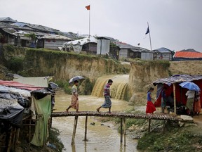 In this photograph taken Aug. 28, 2018, sewer water flows in the back as Rohingya refugees cross a makeshift bamboo bridge at Kutupalong refugee camp, Bangladesh. Access to medical care has changed for the better in the refugee camps in Bangladesh, yet many Rohingya still seek out their faith healers.