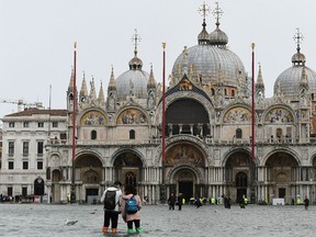 Tourists walk in the flooded Venice land mark Piazza San Marco (Saint Mark Square) during a high-water (Acqua Alta) alert on October 29, 2018 in Venice as the city is inundated by near-record flooding and ferocious storms drove high winds reaching up to 180 kilometres (110 miles) an hour, authorities announced a further six deaths, after confirming five people had died.