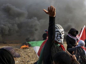 A masked protester chants while others burn tires and waving their national flags near the fence of Gaza Strip border with Israel during a protest east of Gaza City, Friday, Nov. 9, 2018. Gaza's Hamas rulers said Friday that deadly protests along Gaza-Israel perimeter fence have achieved some goals; $15 million from Qatar to help pay the salaries of civil servants.