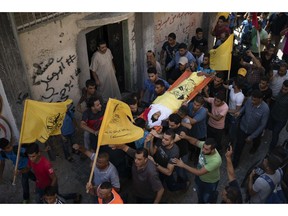 In this Sept. 15, 2018 photo, Palestinians carry the body of 11-year-old Shady Abdel-al during his funeral in Beit Lahiya, northern Gaza Strip. As the boy's body is carried through the neighborhood, it is surrounded by a sea of yellow flags of the Palestinian Fatah party and former guerrilla movement founded by Yasser Arafat. But when it reaches the mosque, there is another huge group of teenagers waiting with the green flag of Hamas.