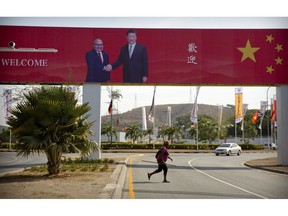 In this Nov. 15, 2018, photo, a woman crosses the street near a billboard commemorating the state visit of Chinese President Xi Jinping in Port Moresby, Papua New Guinea. As world leaders arrive in Papua New Guinea for a Pacific Rim summit, the welcome mat is especially big for China's President Xi Jinping. With both actions and words, Xi has a compelling message for the South Pacific's fragile island states, long both propped up and pushed around by U.S. ally Australia: they now have a choice of benefactors.