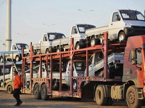 In this Oct. 31, 2018, photo, a staff members walks past a semi truck loaded with new vehicles in the parking lot for a local automaker in Qingdao in eastern China's Shandong province. China's auto sales sank for a fourth month in October, tumbling 13 percent from a year earlier and adding to an unexpectedly painful downturn for global automakers in their biggest market. (Chinatopix via AP)