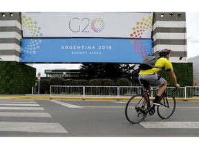 A man rides a bicycle past a banner promoting the G20 summit at the Costa Salguero Center, in Buenos Aires, Argentina, Tuesday, Nov. 27, 2018. Thousands of police and security agents will guard the Group of 20 industrialized nations' world leaders during the two-day meeting that starts Friday.