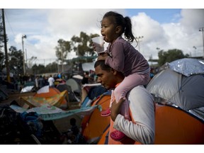 A man carries a girl on his shoulders at a migrant shelter in Tijuana, Mexico, Thursday, Nov. 22, 2018. Several thousand Central American migrants arrived in Tijuana last week more than a month after leaving Honduras in a caravan.