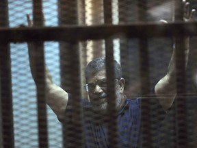 FILE - In this May 16, 2015 file photo, ousted Egyptian President Mohammed Morsi raises his hands as he sits behind glass in a courtroom, at the national police academy in a Cairo suburb, Egypt. On Wednesday, Dec. 26, 2018, two former Egyptian presidents appeared in the same Cairo courtroom. The 90-year-old Mubarak testified in a retrial of Mohammed Morsi. Mubarak whose nearly three-decade rule was ended by a popular uprising in 2011, was seen walking into the courtroom with a cane along with his two sons Alaa and Gamal.