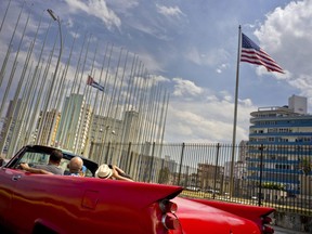 Tourists ride a vintage American convertible as they drive next to the American flag and a Cuban flag at the United States embassy in Havana, Cuba, Friday, March 18, 2016.