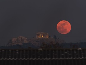 FILE - In this Wednesday, Jan. 31, 2018 file photo a super blue blood moon rises behind the 2,500-year-old Parthenon temple on the Acropolis of Athens, Greece.