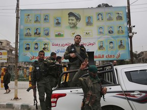 FILE - In this March 28, 2018 file photo, members of the Kurdish internal security forces stand on their vehicle in front of a giant poster showing portraits of fighters killed fighting against the Islamic State group, in Manbij, north Syria. On Friday, Dec. 28, 2018, Syria's military announced it has taken control the flash-point Kurdish-held town of Manbij, where Turkey has threatened an offensive. The announcement Friday came shortly after the main Syrian Kurdish militia invited the government to seize control of Manbij to prevent an attack.