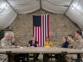 President Donald Trump, accompanied by National Security Adviser John Bolton, third from left, first lady Melania Trump, fourth from right, US Ambassador to Iraq Doug Silliman, third from right, and senior military leadership, speaks to members of the media at Al Asad Air Base, Iraq, Wednesday, Dec. 26, 2018.