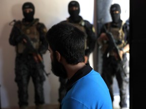 In this file picture taken on Friday, July 21, 2017, Kurdish soldiers from the Anti-Terrorism Units, background, stand in front a blindfolded man, a suspected Islamic State member at a security center, in Kobani, Syria.