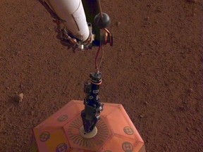 This photo provided by NASA Jet Propulsion Laboratory, shows the new Mars lander placing a quake monitor on the planet's dusty red surface.  The unprecedented milestone occurred less than a month after Mars InSight's touchdown. InSight's robotic arm removed the seismometer from the spacecraft deck and set it directly on the ground Wednesday, Dec. 19, 2018 to monitor Mars quakes.(NASA Jet Propulsion Laboratory via AP)