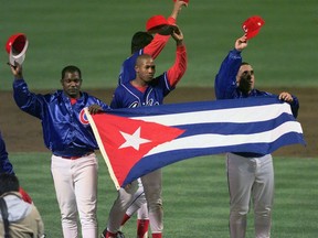 FILE - In this Monday, May 3, 1999 file photo, members of the Cuban baseball team carry their country's flag onto the field after a baseball game against the Baltimore Orioles at Camden Yards in Baltimore. Major League Baseball, its players' association and the Cuban Baseball Federation reached an agreement that will allow players from the island nation to sign big league contracts without defecting, an effort to eliminate the dangerous trafficking that had gone on for decades. The agreement runs through Oct. 31, 2021.