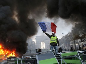FILE - In this Nov. 24, 2018 file photo, a demonstrator waves the French flag on a burning barricade on the Champs-Elysees avenue with the Arc de Triomphe in background, during a demonstration against the rise of fuel taxes. Across the world, people are questioning truths they had long held to be self-evident, and they are dismissing some of them as fake news. They are replacing traditions they had long seen as immutable with haphazard reinvention. In France, people who feel left behind by a globalizing world have spent the last few weeks marching and rioting to protest a government they call elitist and out of touch.