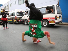 In this Dec. 12, 2018 photo, Venezuelan Karin Rojas balances on her head as she breakdances with Angel Fernandez for tips from commuters in Lima, Peru. Rojas, 25, arrived in Lima in 2016, leaving behind her mountainous home in the Venezuelan state of Merida, where she ran a break dancing collective with her husband.