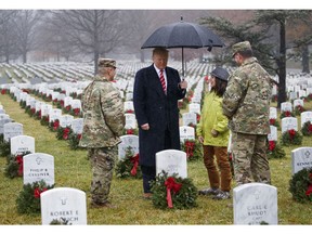 President Donald Trump pauses in the rain among holiday wreaths at graves at Arlington National Cemetery in Arlington, Va., Saturday, Dec. 15, 2018, during Wreaths Across America Day. Wreaths Across America was started in 1992 at Arlington National Cemetery by Maine businessman Morrill Worcester and has expanded to hundreds of veterans' cemeteries and other locations in all 50 states and beyond.