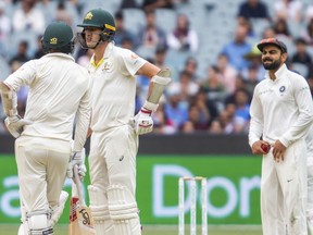 Australia's Nathan Lyon, left, and Pat Cummins, center, at the end of an over speak as India's Virat Kohli looks on during play on day five of the third cricket test between India and Australia in Melbourne, Australia, Sunday, Dec. 30, 2018.